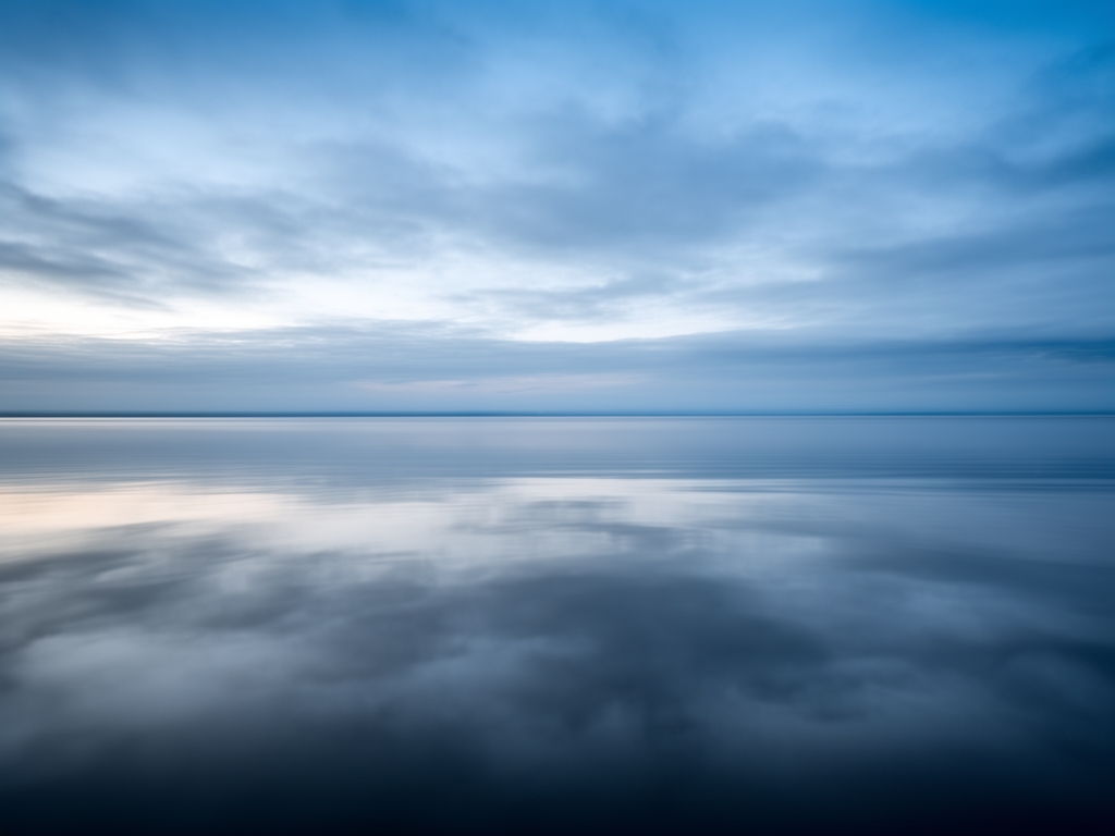 Lugnt vattenyta med perfekt spegling av himlen i vackert blå och grå nyanser – minimalistisk och meditativ bild som förmedlar ro och klarhet